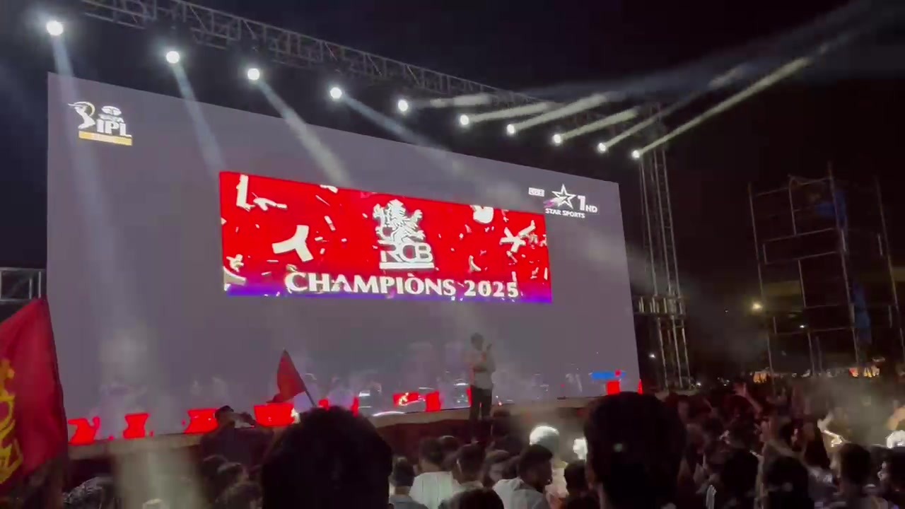 Crowd watching an IPL final on a large open-ground LED wall under beam lights
